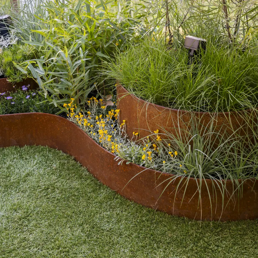 Curved rust-brown steel edge dividing lawn from a bed of grasses and yellow flowers