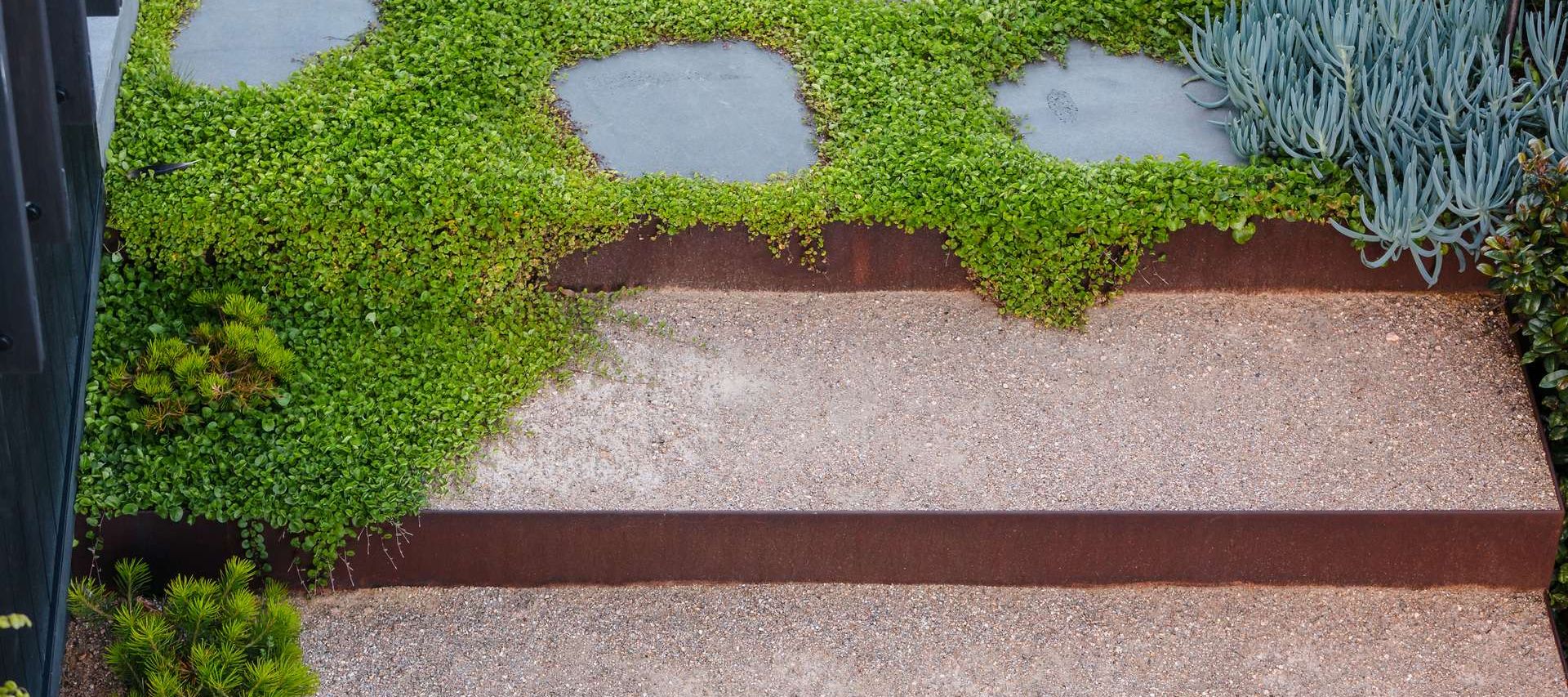 Stepped garden terraces edged in rust-brown steel, with gravel treads and stepping stones